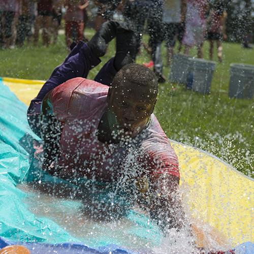Dushawn Darling slides down a slip and slide during the annual Holi Celebration outside of Ford Center for the Fine Arts. 
