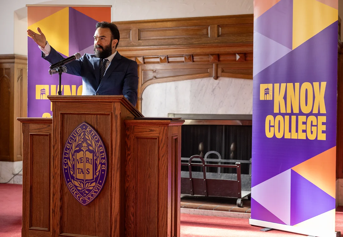 A Knox Alumni Achievement Award winner gestures from the podium. He is framed by multicolor banner that says "Knox College."