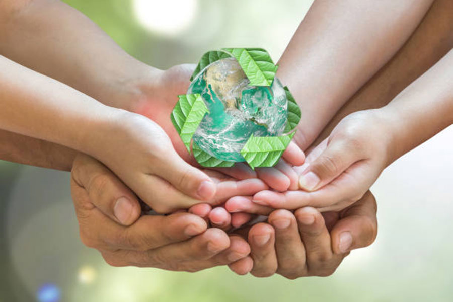 Several hands helping hold up a small world with the recycle symbol over it.