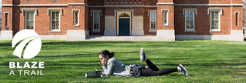 A Knox College student enjoys a beautiful day reading on the south lawn of Old Main