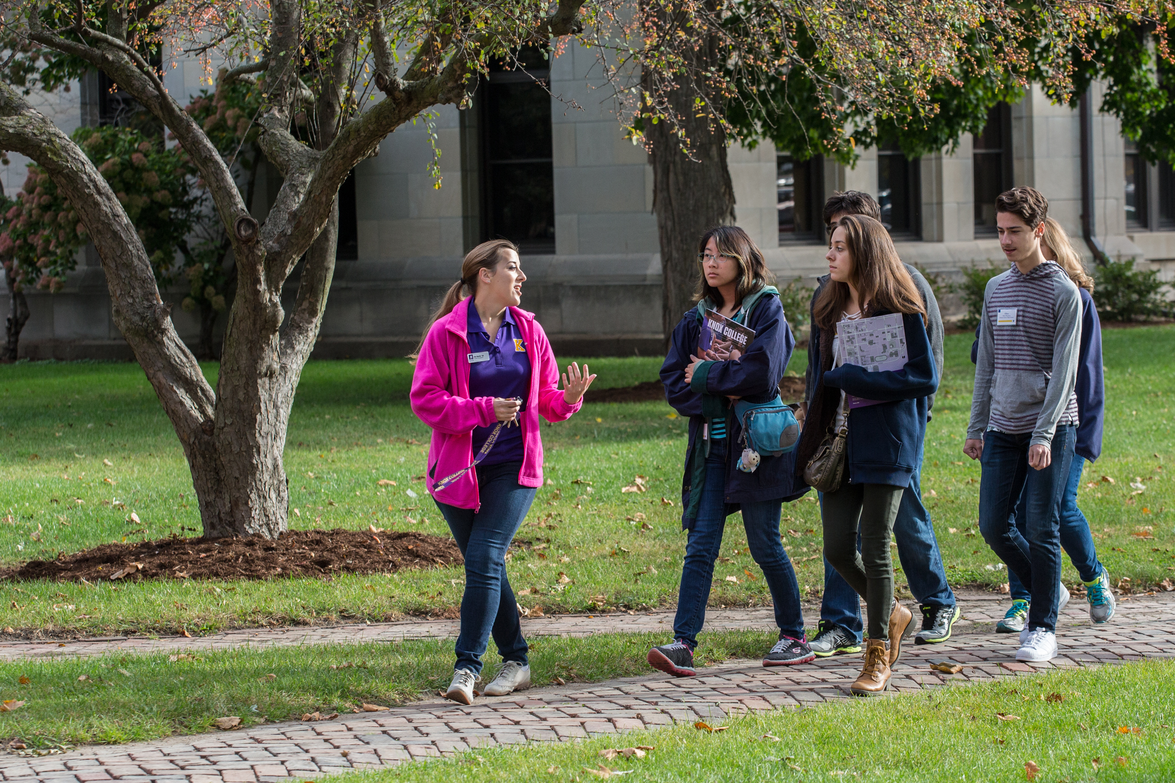 A tour guide leads a group of visitors down the sidewalk on the Knox College campus.