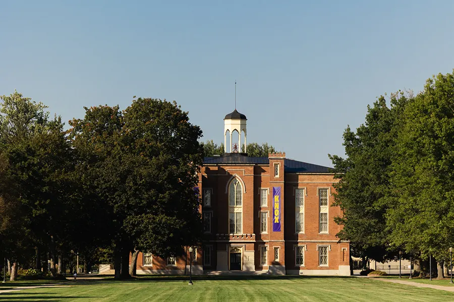 Surrounded by trees, Old Main stands against a blue sky. 