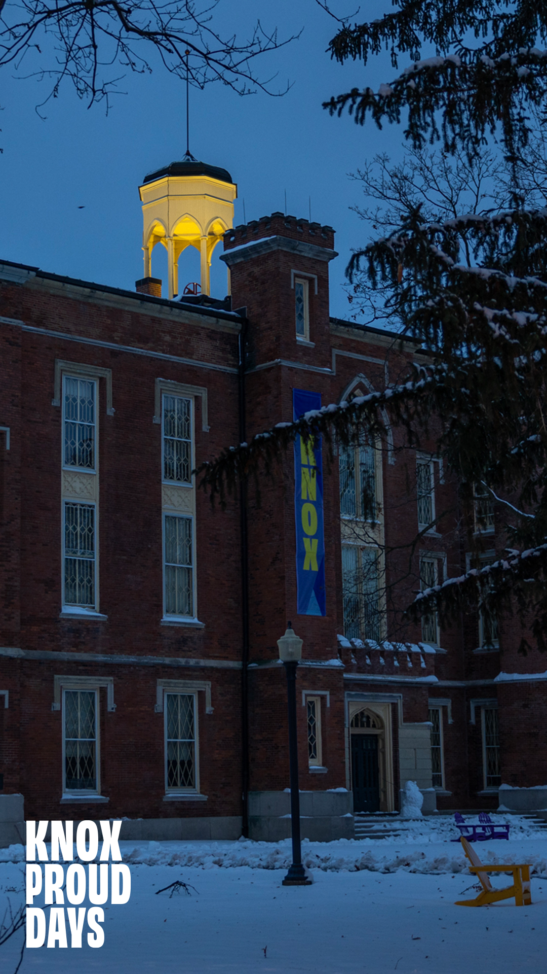 A winter scene outside of Old Main. Snow is visible on the ground and it is a night time scene. Knox Proud Days is visible in the bottom left corner.