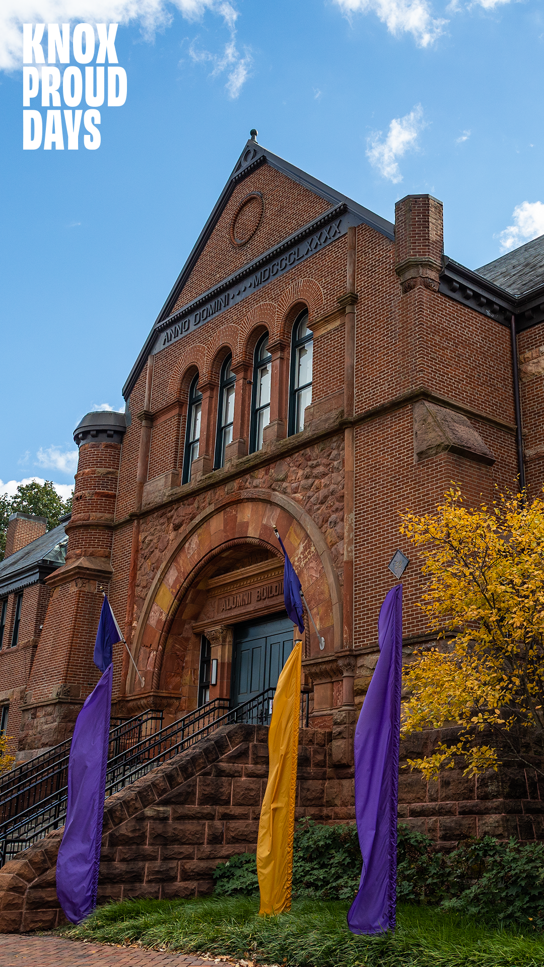 A brick building with purple flags in the foreground. There is a bright blue sky with Knox Proud Days in the top left corner.