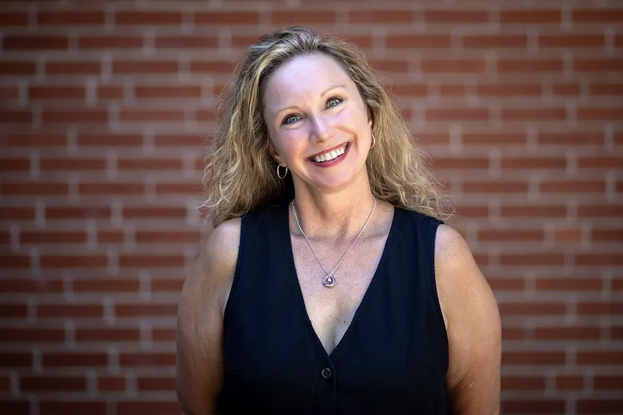 Kate Konecky smiles at the camera, a brick wall behind her. 