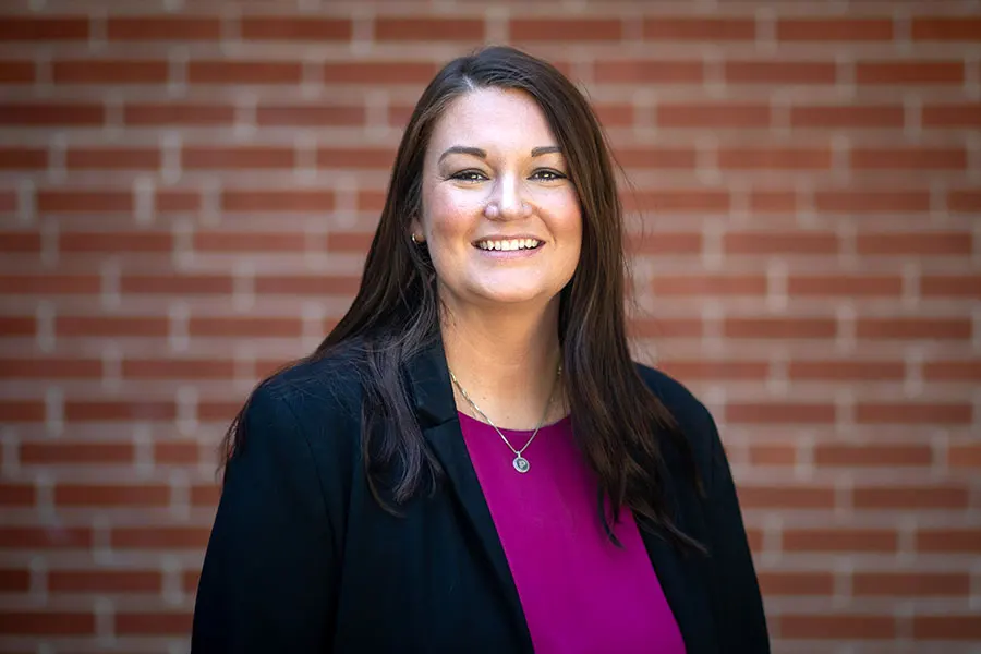 Shelby Schwieter smiles at the camera, a brick wall serves as the background behind her.