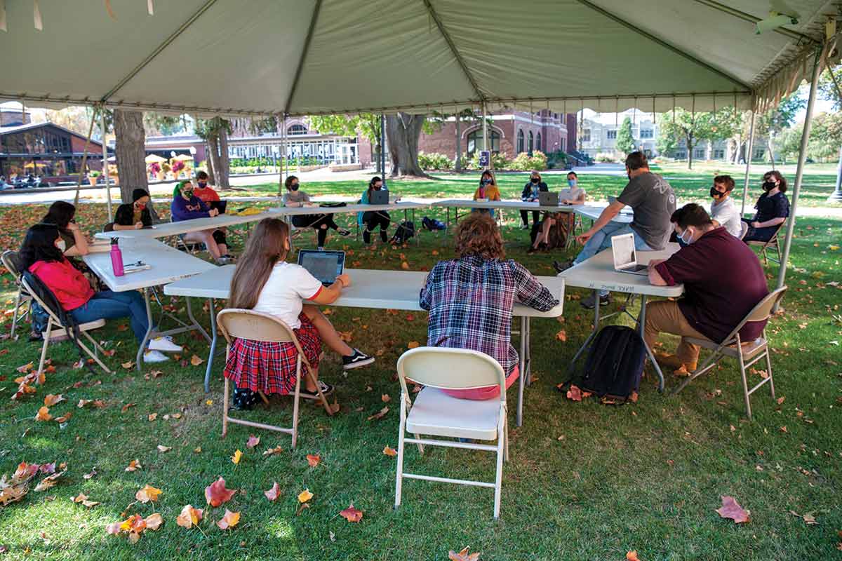 A group of students gather at tables under a tent on the South Lawn during the fall 2020 term.