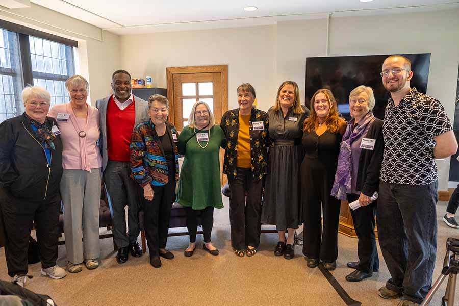 A group of 10 people stand lined up next to each other, embracing each other, and smiling for a photo.