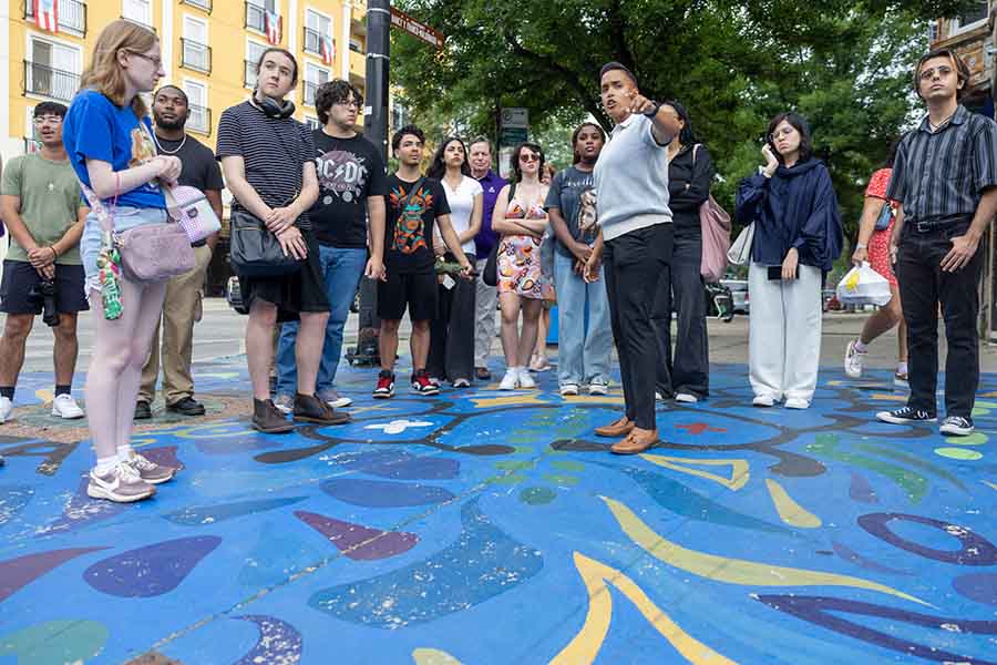 A group of students stand around an alderperson who is giving them a tour of the neighborhood in Chicago.