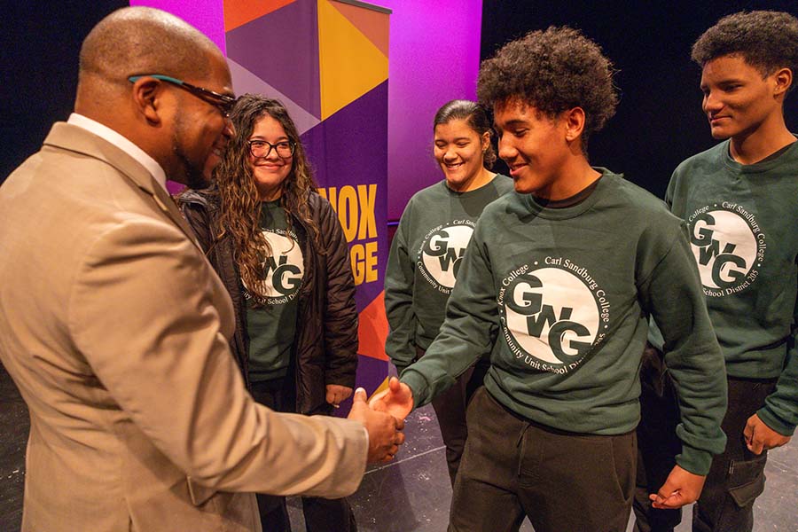 A student shakes a man's hand with a group of students standing behind him.