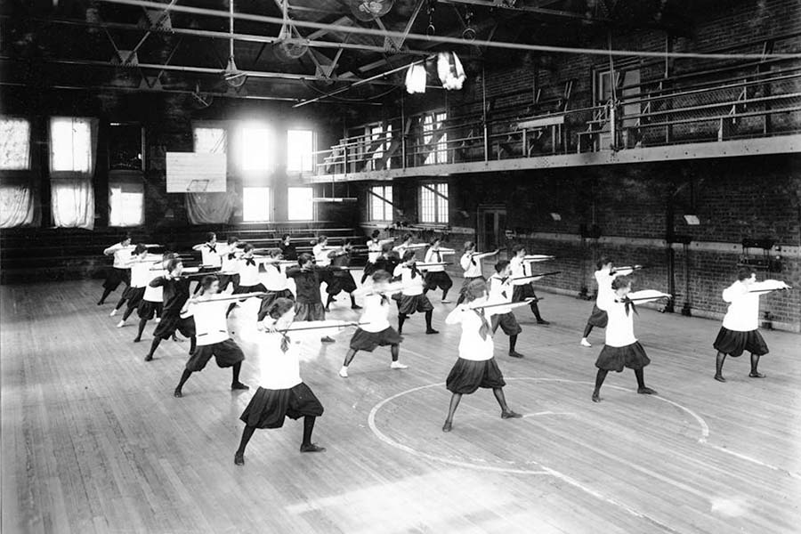 A black and white photo of a class of students in the aux gym.