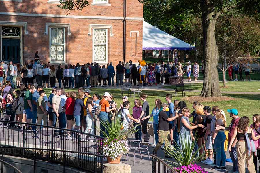 Two lines of people outside facing each other, everyone is shaking hands with each other.