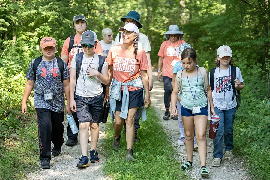 A group of students and instructors go for a hike outside on a sunny day surrounded by trees.