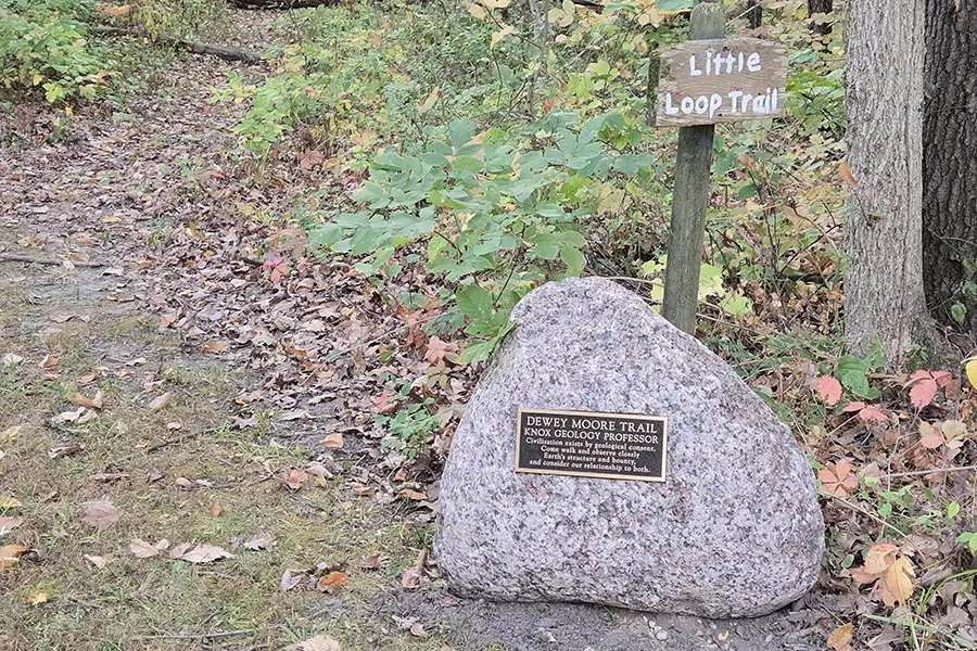 A trail marker honoring Dewey Moore sits on the trail with a sign above it.