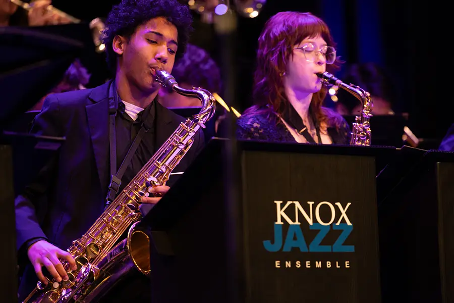 Two students play the saxophone in front of a stand that says Knox Jazz.