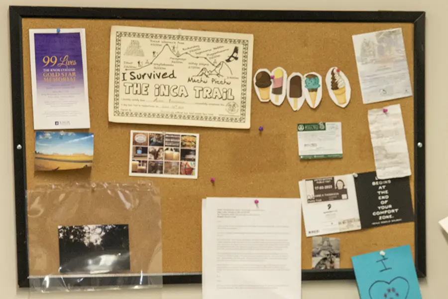 A bulletin board hangs on the wall with various pieces of paper pinned to it.