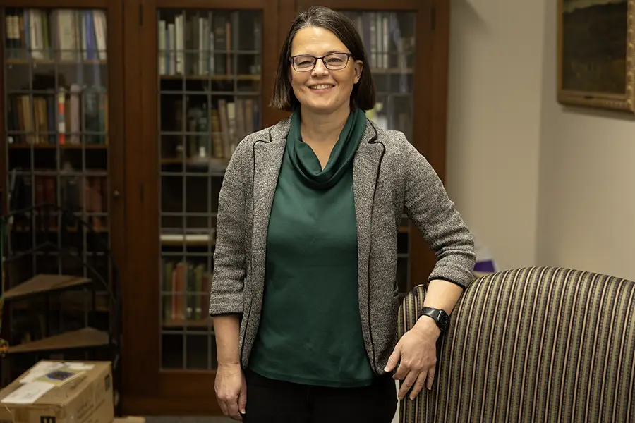 Director of the Library Anne Thomason stands in her office with her hand on her chair.