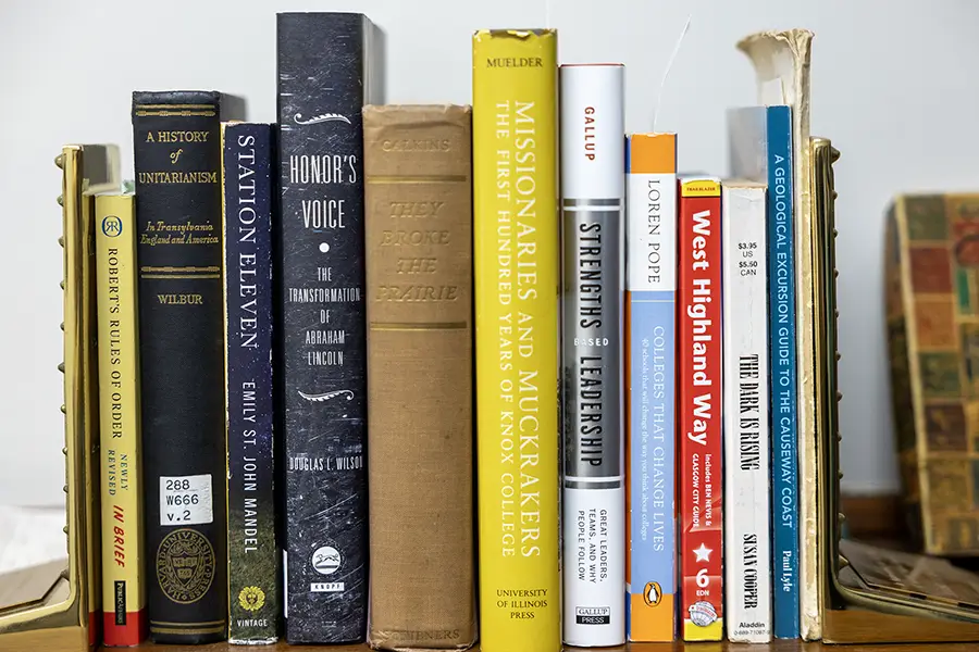 Different color books sit on a mantle in a line.