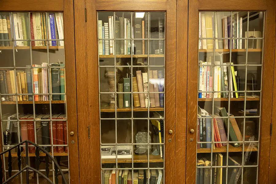 A large cabinet sits in the office full of books.