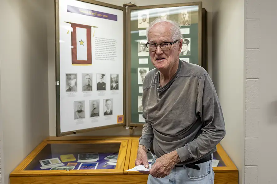 Jamie Bjorkman ’57 stands in front of the 99 Lives Gold Star Memorial exhibit in Knox’s Memorial Gymnasium.