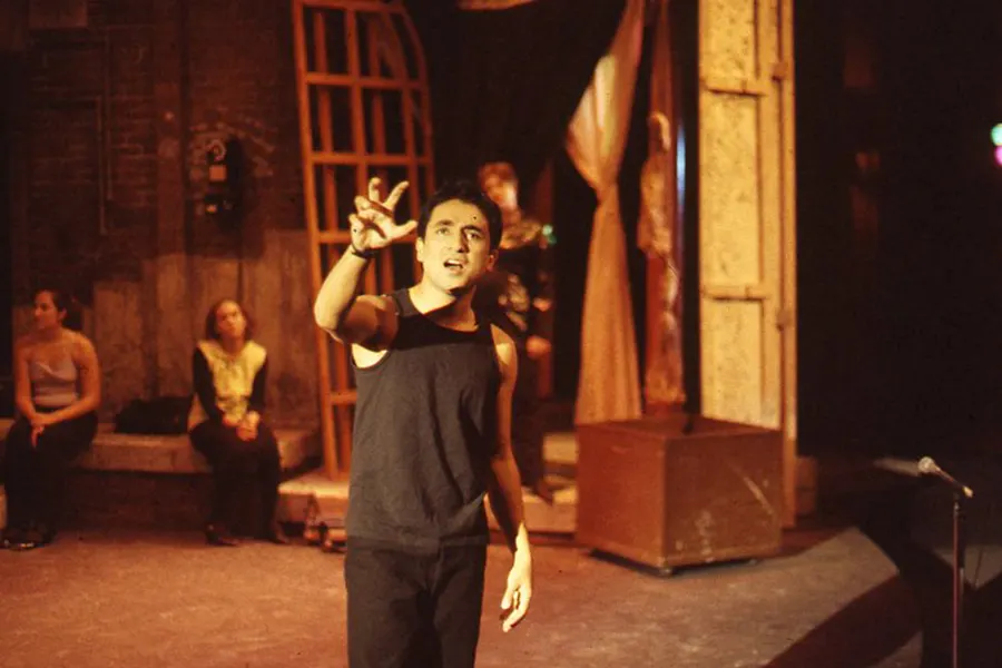 Performing in a Knox Theatre production, Vir Das faces the camera. His hand forms a claw as he speaks, the stage behind him.
