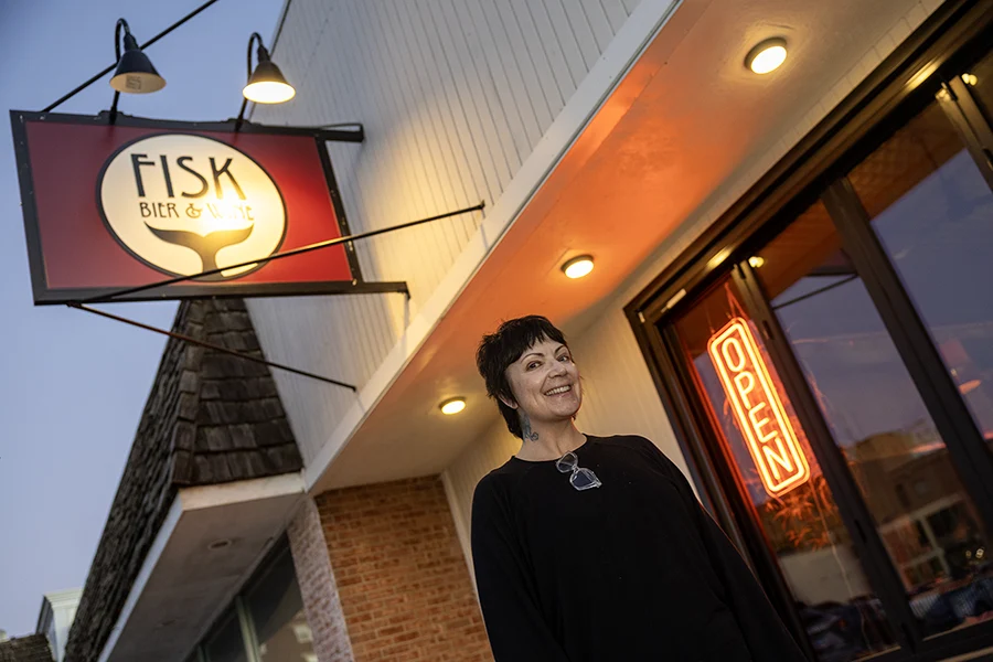 Kelly Fisk stands outside Fisk Bier & Wine. A neon OPEN light is visible behind her.