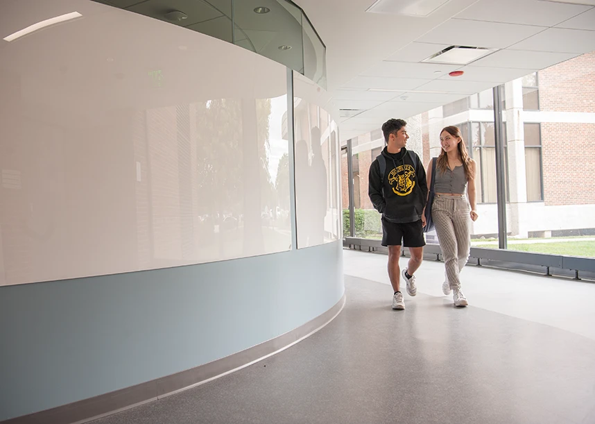 Two Knox students walk down a windowed hallway in the Umbeck Science-Mathematics Center.