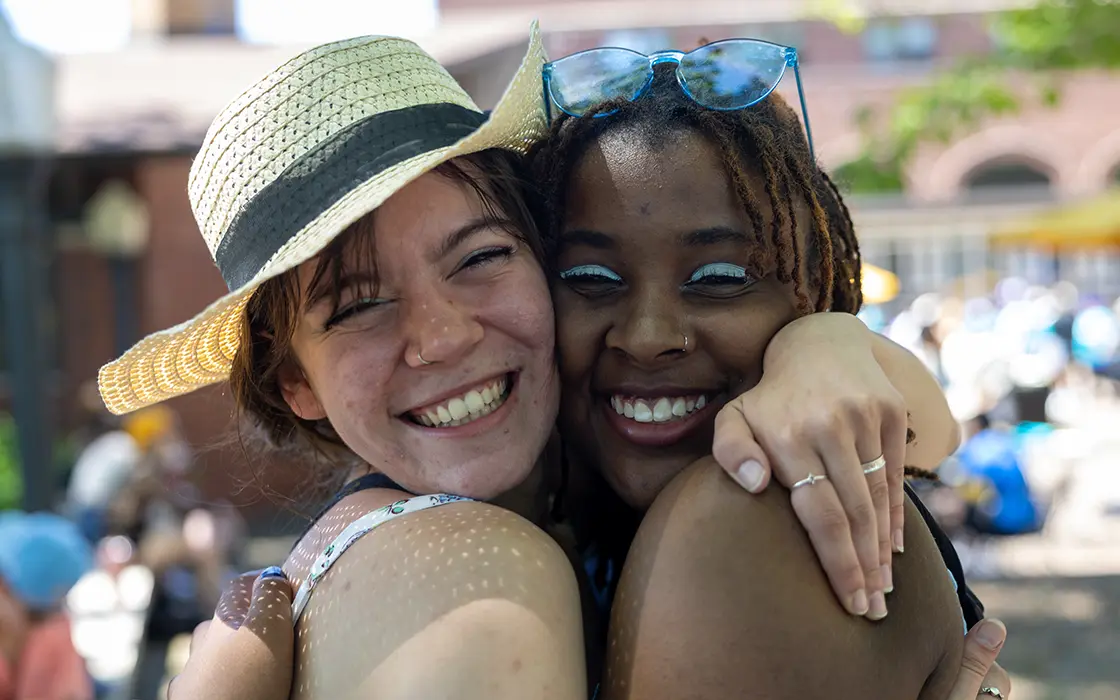 Two smiling students embrace each other in a hug.