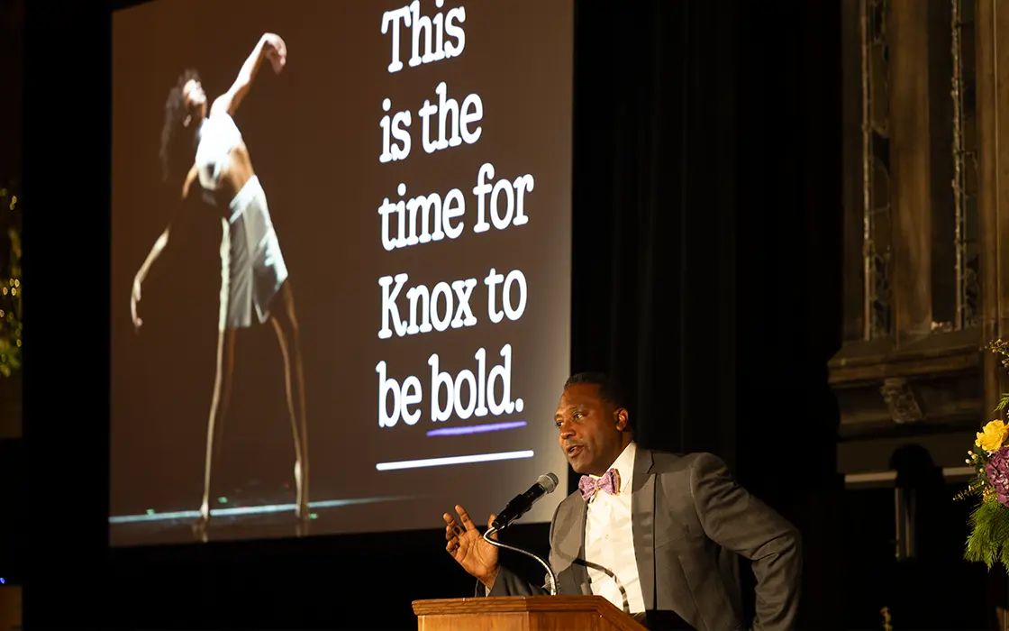 Knox President Andrew McGadney speaks at a podium in front of a slide that says "This is the time for Knox to be bold" and features a student dancer.