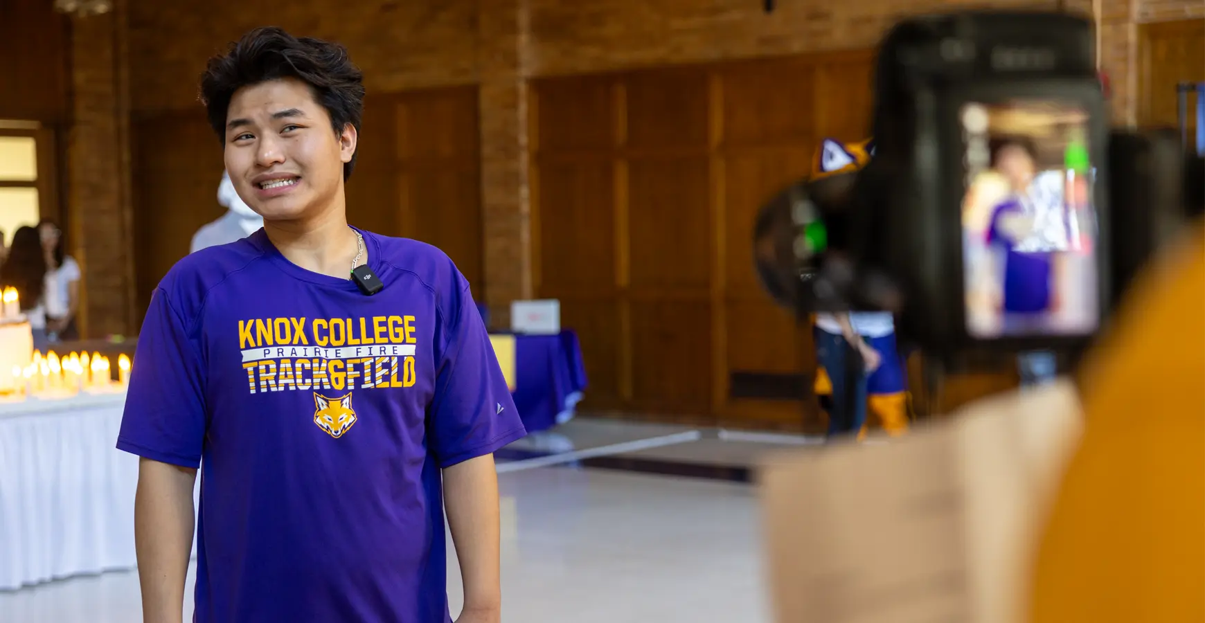 A student grins as his photo is taken. A cake with candles is visible in the background.