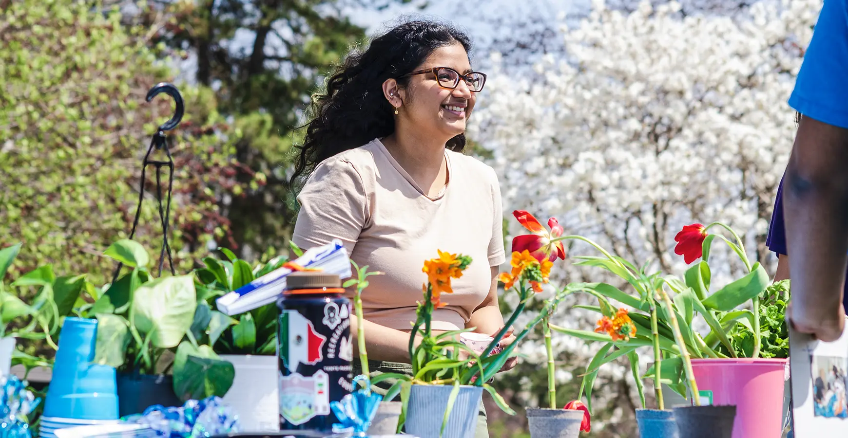 A Knox student sales an assortment of plans during Earth Month. Flowering trees are behind her table.