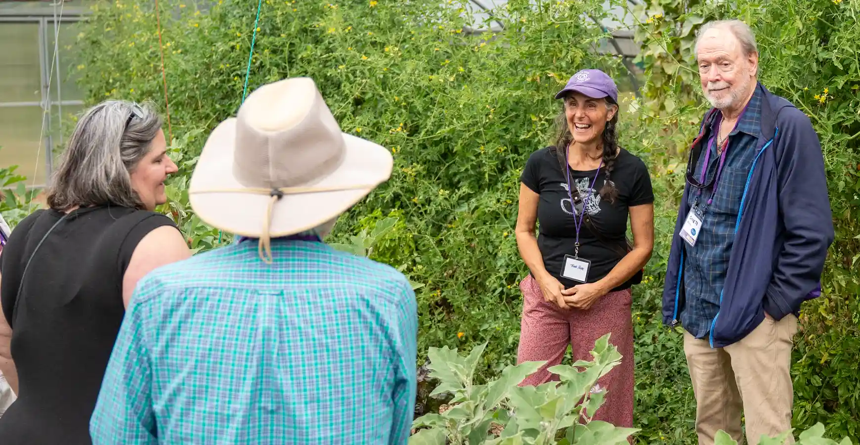 A group of people talk, surrounded by plants and greenery.