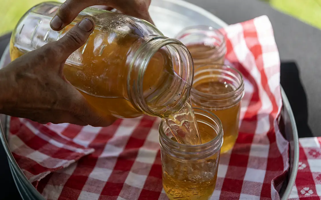 Hands holding a quart jar and pouring tea into a glass. 