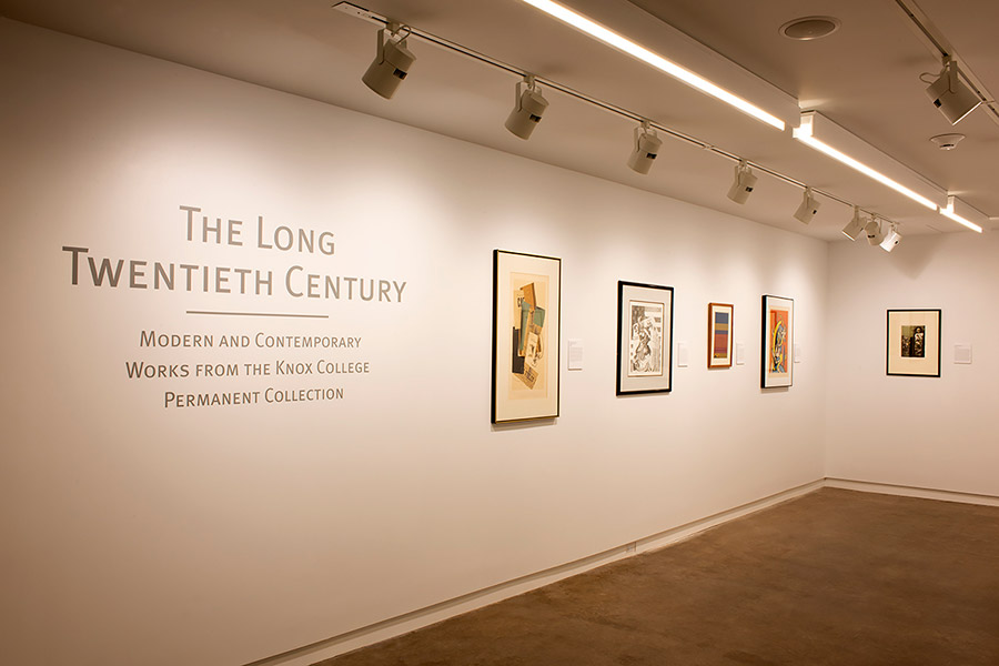 Works of art hang on the wall in an art gallery. Text on the wall says: The Long Twentieth Century—Modern and Contemporary Works from the Knox College Permanent Collection.