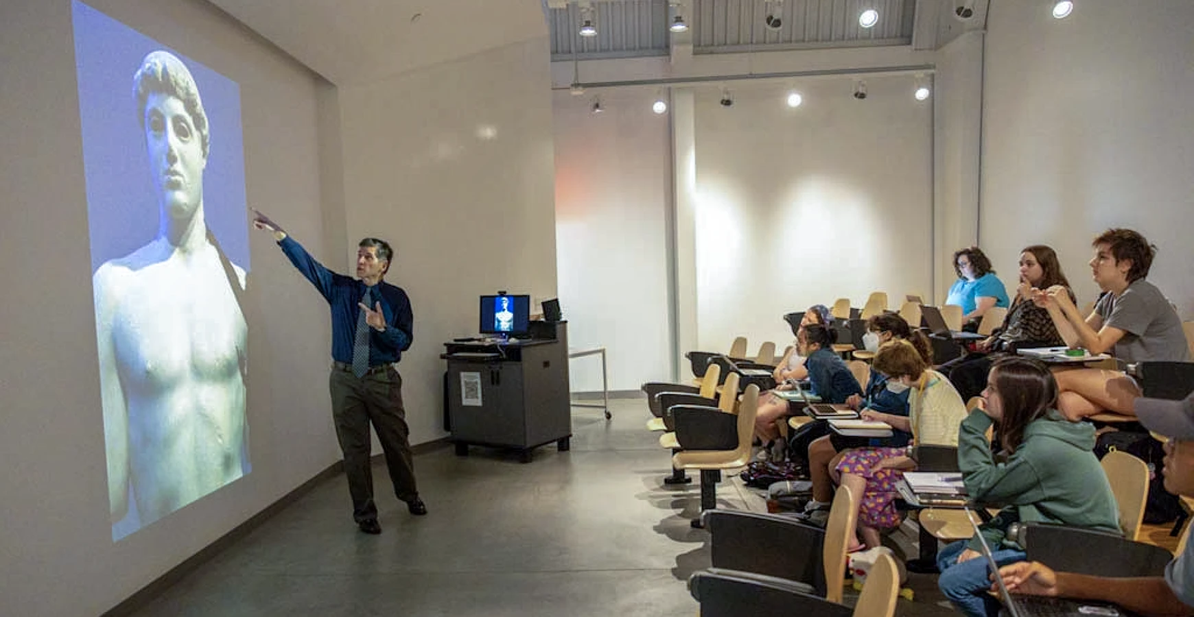 Art History professor Greg Gilbert points at a projected image of a classical Roman statue in the Whitcomb Art Center Art History lecture hall; students look on.