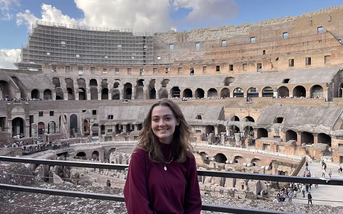 A student smiles at the camera; the Colosseum is in the background.