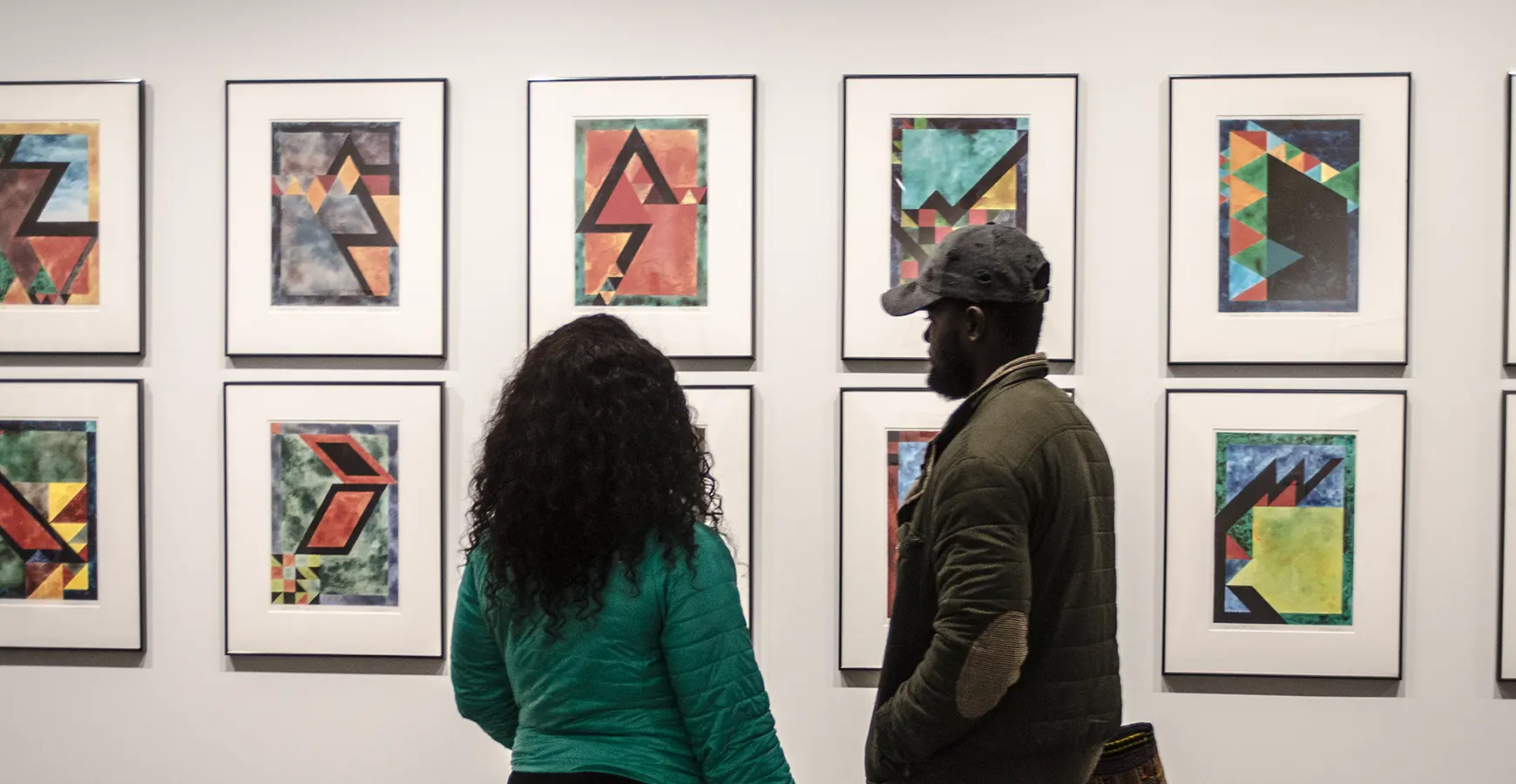 Two people look at a wall of framed art.