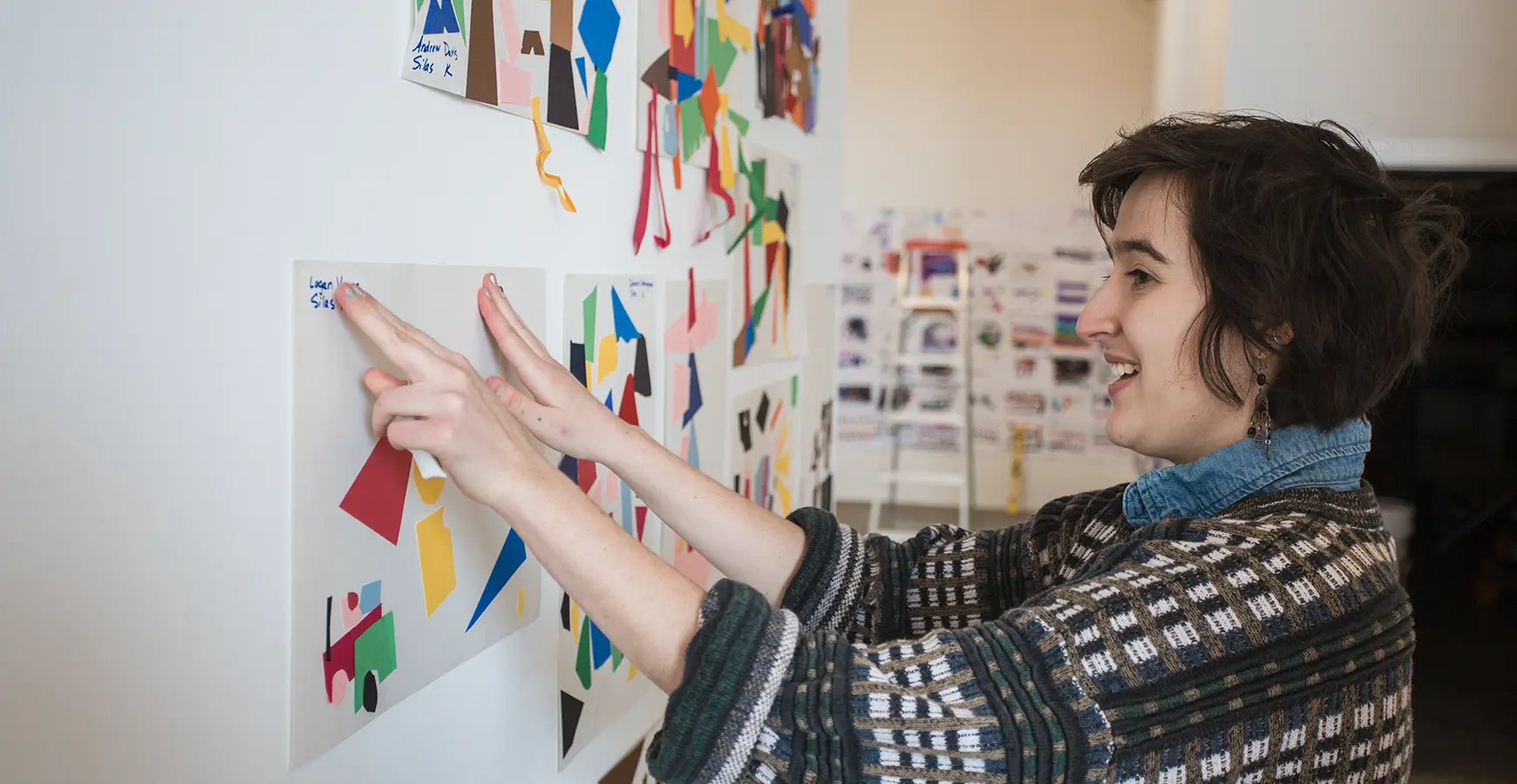 A student presses the edges of a piece of art to hang it on a wall, alongside similar pieces of art.