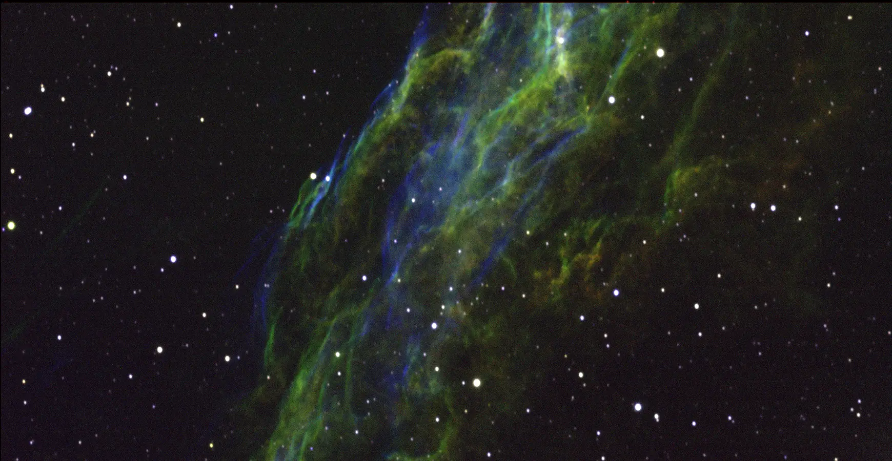 Image taken through a telescope. Stars are visible with wisps of green and blue colors in the center.