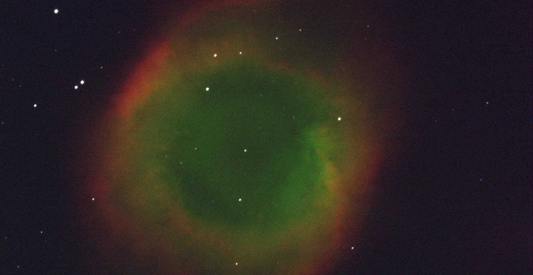 Image taken through a telescope. Stars are visible with a circle of green, yellow, and red in the center.