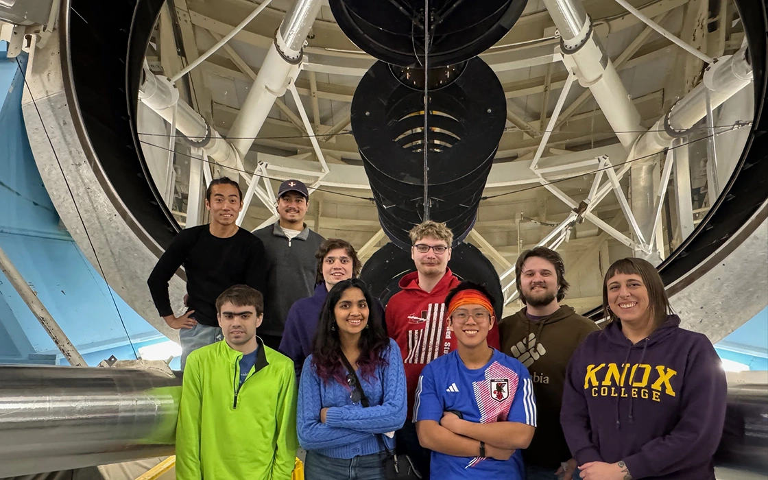 A group of students stand with Professor Nathalie Haurberg in front of a large telescope.