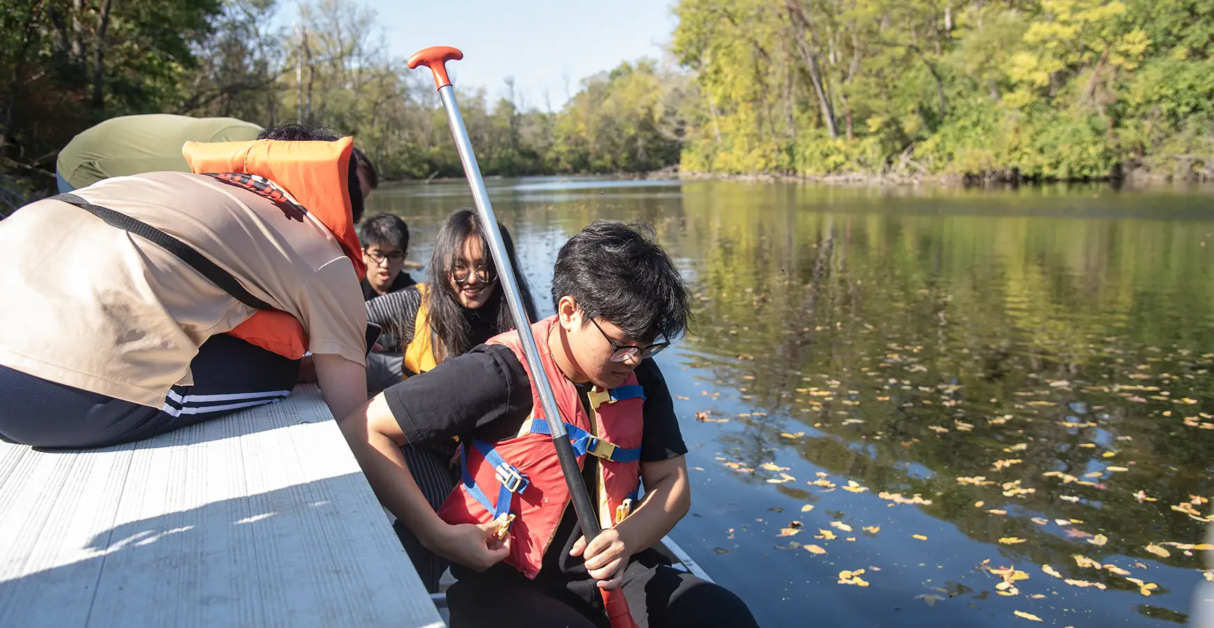 Three students wearing life vests in a canoe on the lake at Green Oaks.