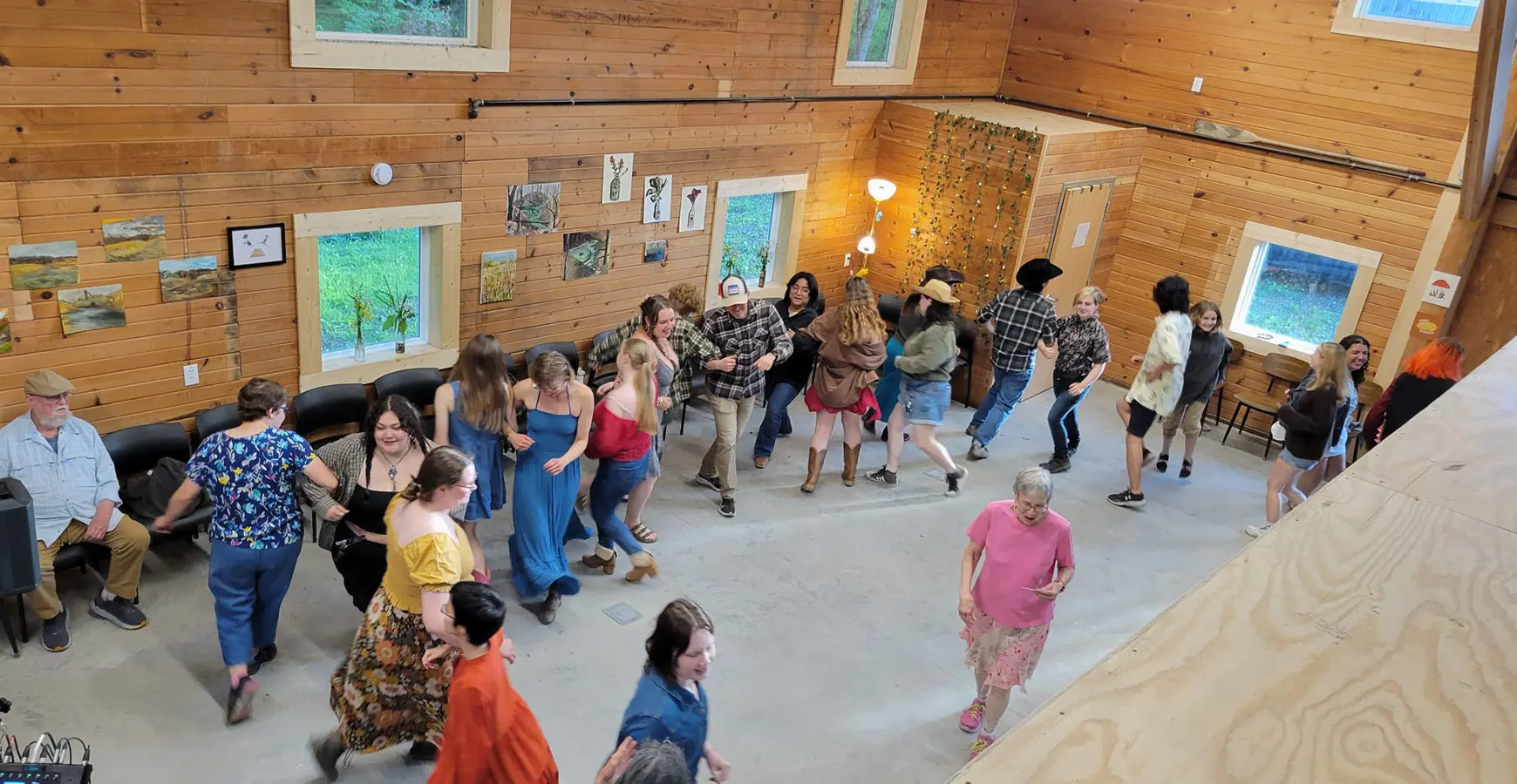 View from above—a crowd dances in a building with large windows, cement floors, and walls covered with pine.