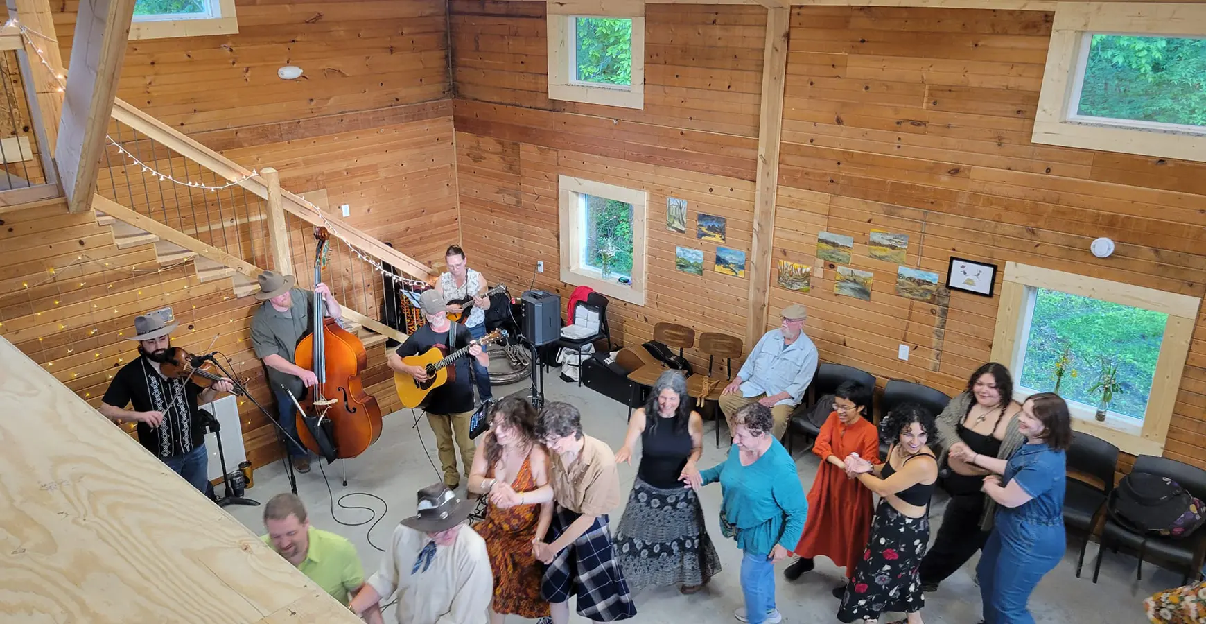 View from above—a crowd dances in a building with large windows, cement floors, and walls covered with pine.