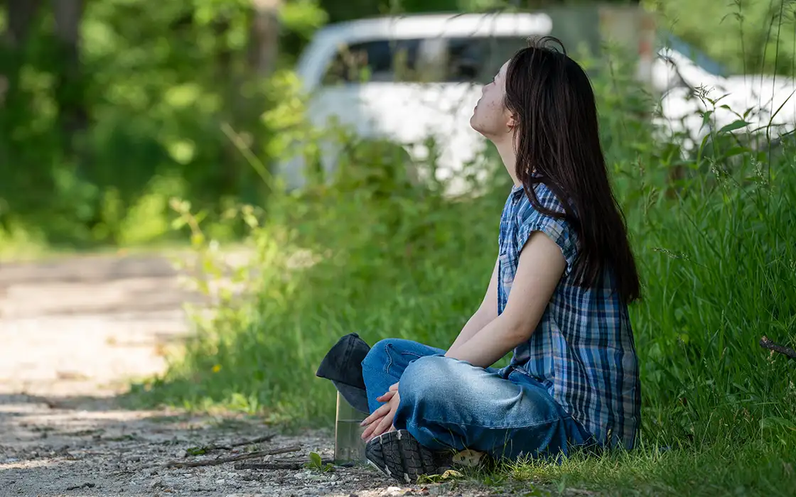 A student sits crosse legged on the ground at Green Oaks, Knox's prairie campus. Her eyes are closed, and she is looking up to the sky.