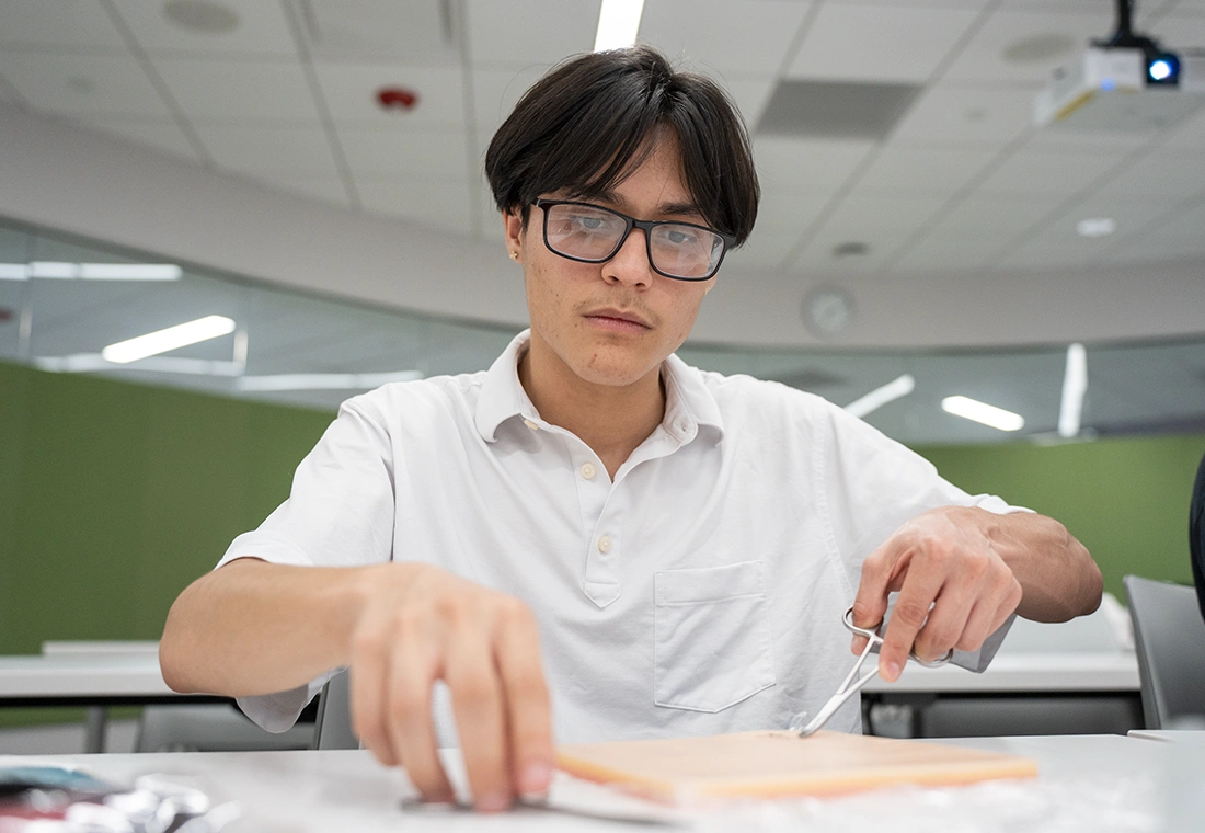 A student wearing safety glasses dissects a specimen in a biology lab.