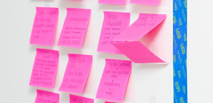 Pink post-it notes are stuck on a white wall. All the notes have handwriting on them, and the closest note says easy to navigate site.