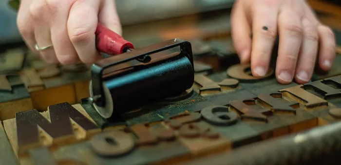 Hands rolling ink over letterpress wood block type