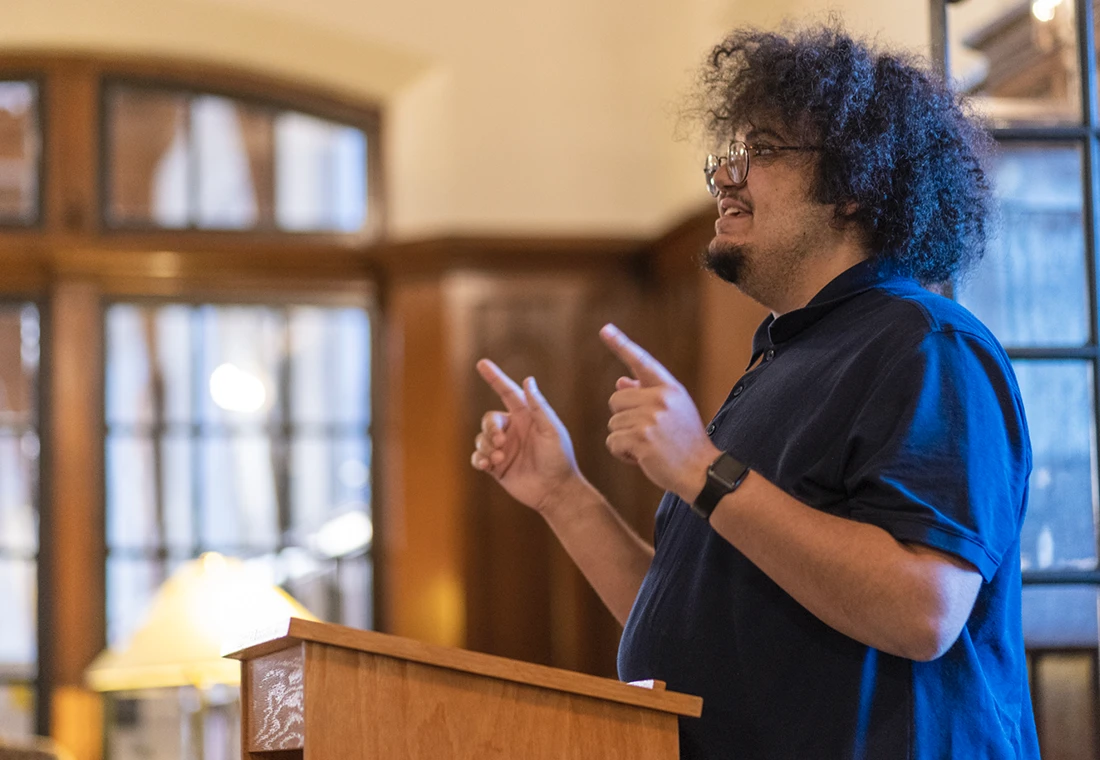 A student stands at a podium in Seymour Library, speaking during Milk Route.