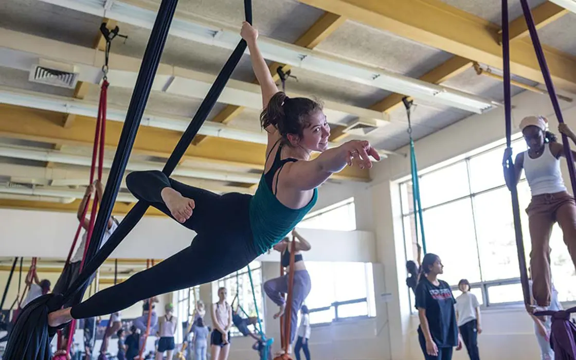In a dance studio, a dance student strikes a dance pose, suspended in air by ropes.